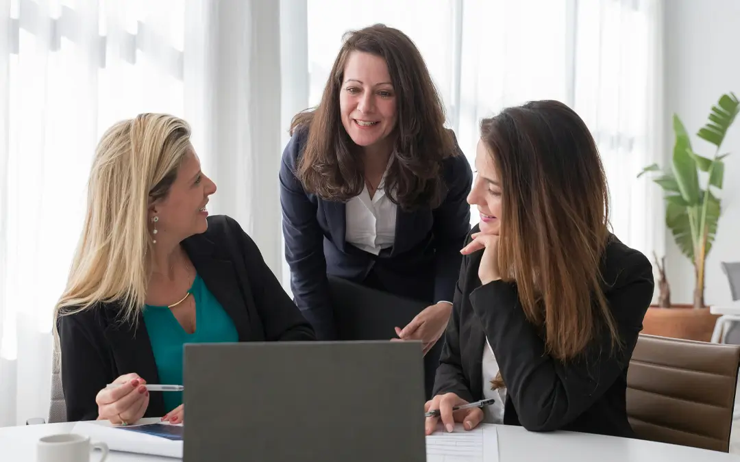 três mulheres conversando frente a um laptop