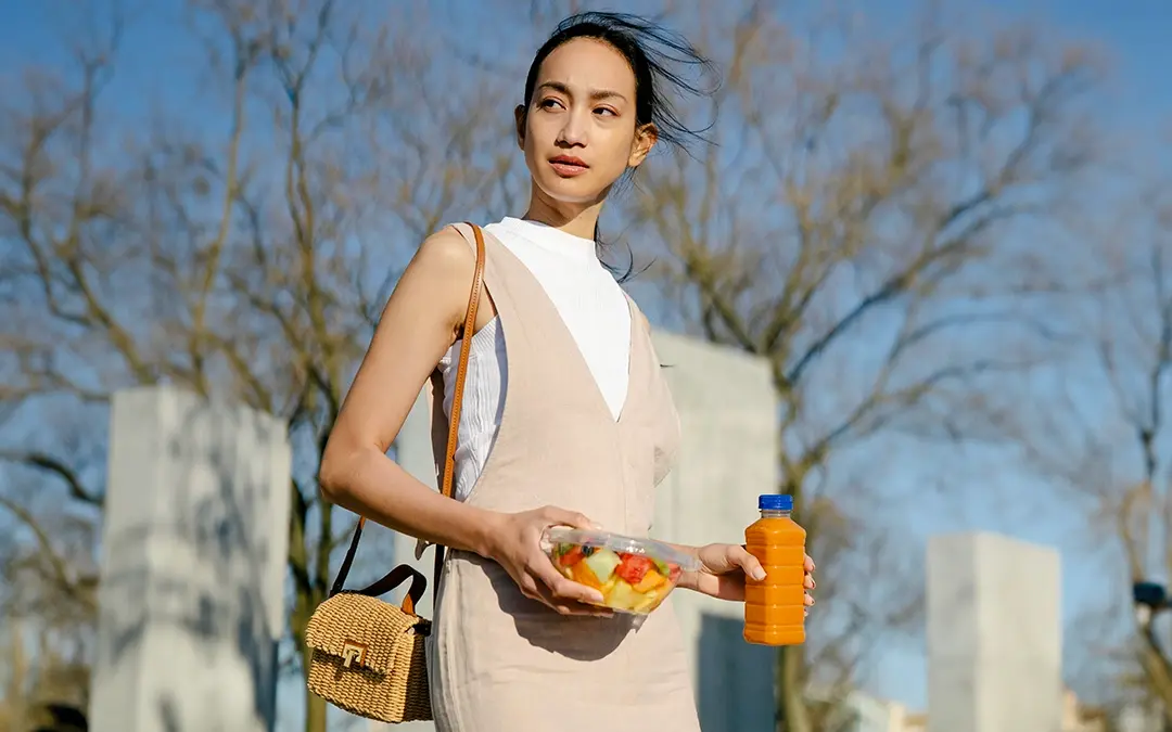 mulher no horário de almoço segurando embalagem de frutas e suco