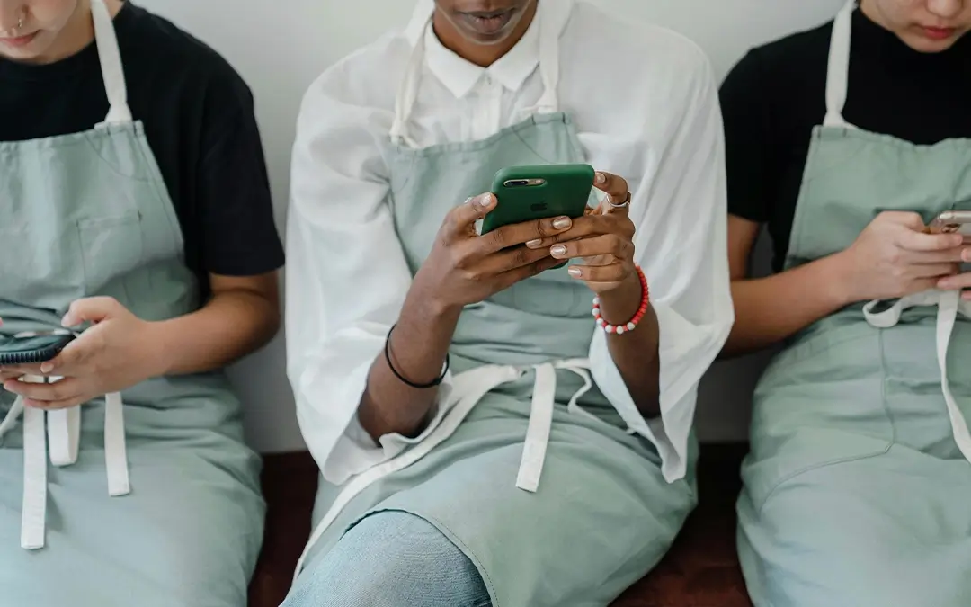 três funcionárias sentadas mexendo nos celulares