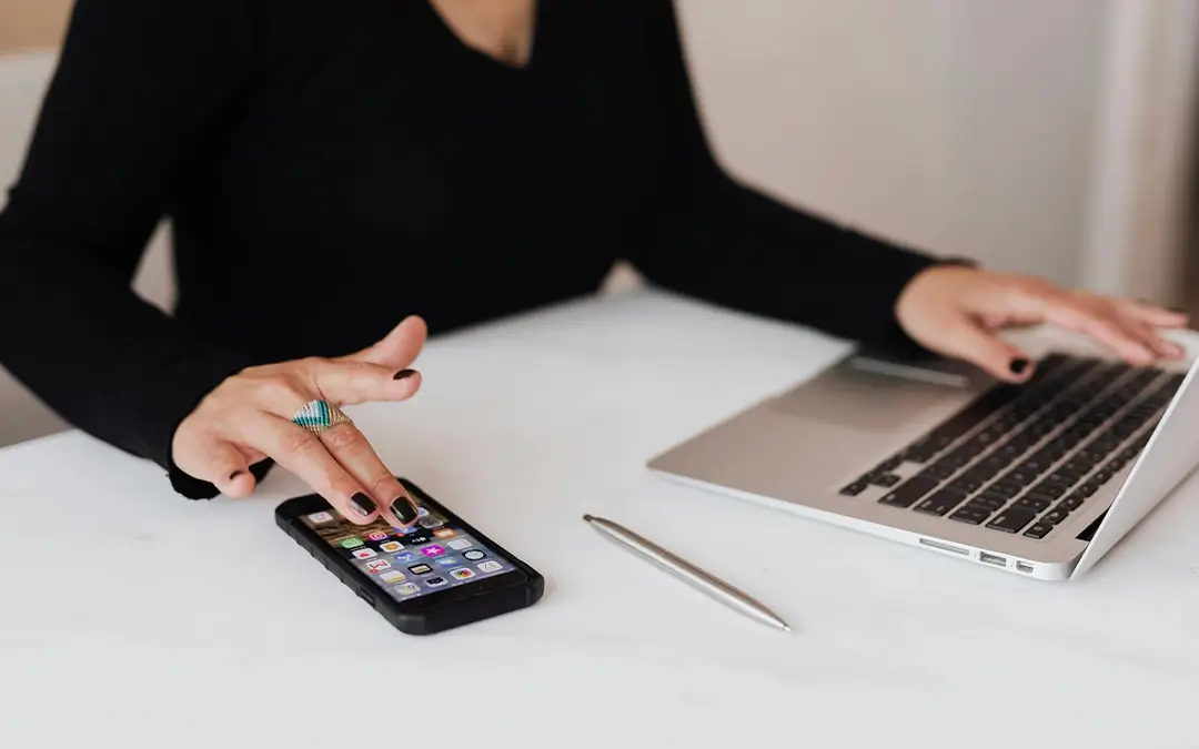 mulher trabalhando no laptop e mexendo no celular