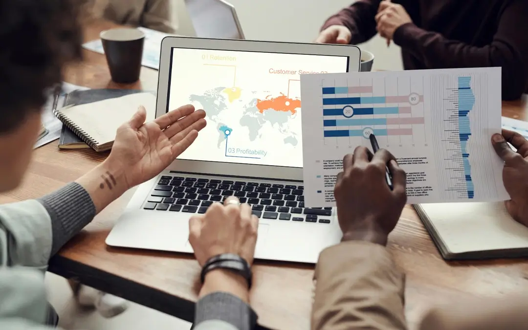 pessoas de costas analisando gráficos em papel e no laptop