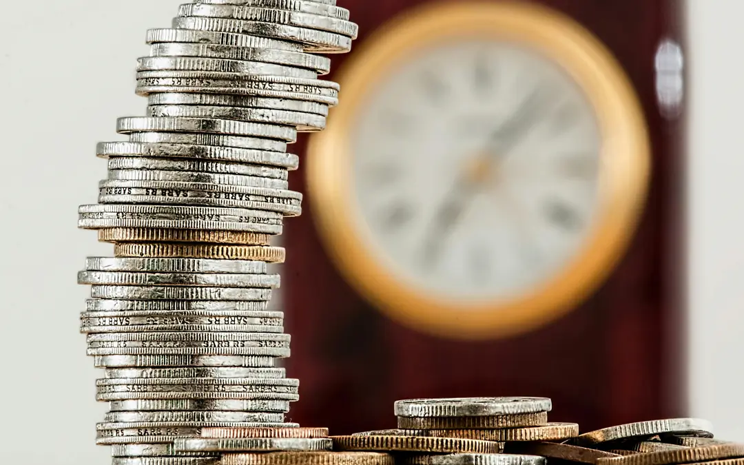 pilha de moedas com relógio desfocado ao fundo