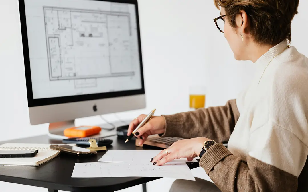 mulher, arquiteta, de meia idade, fazendo anotações de frente com projeto no computador