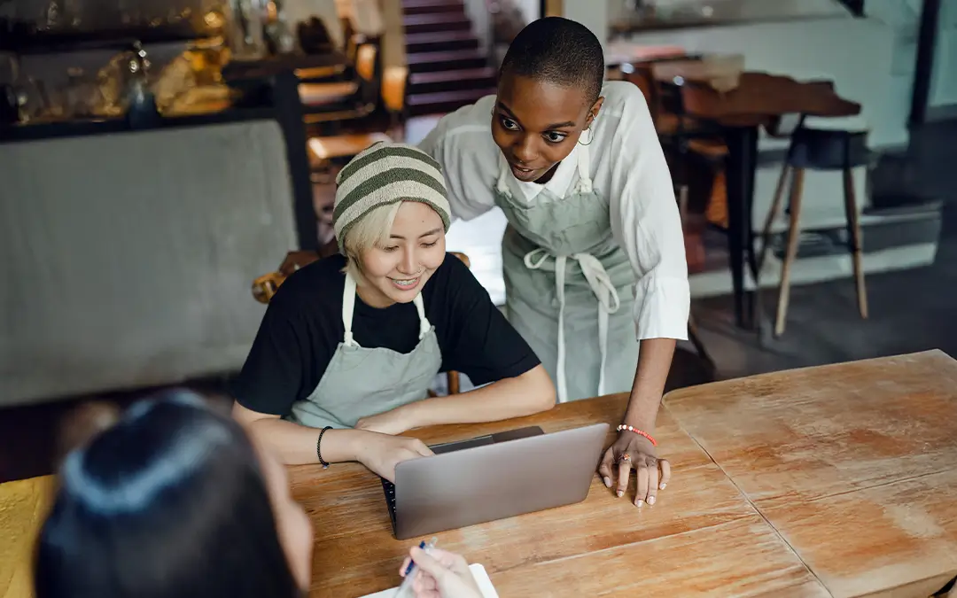 duas mulheres, chefs de cozinha, de frente com laptop conversando com cliente