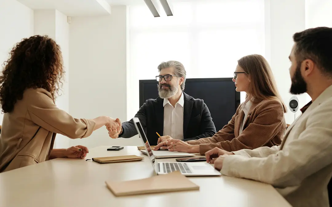 Homem cumprimentando nova funcionária junto de outros entrevistadores.