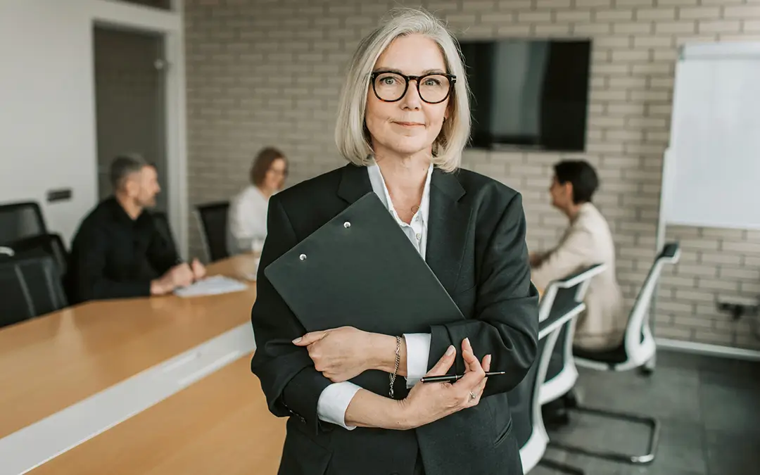 mulher de meia idade segurando pasta com curriculos com equipe conversando ao fundo