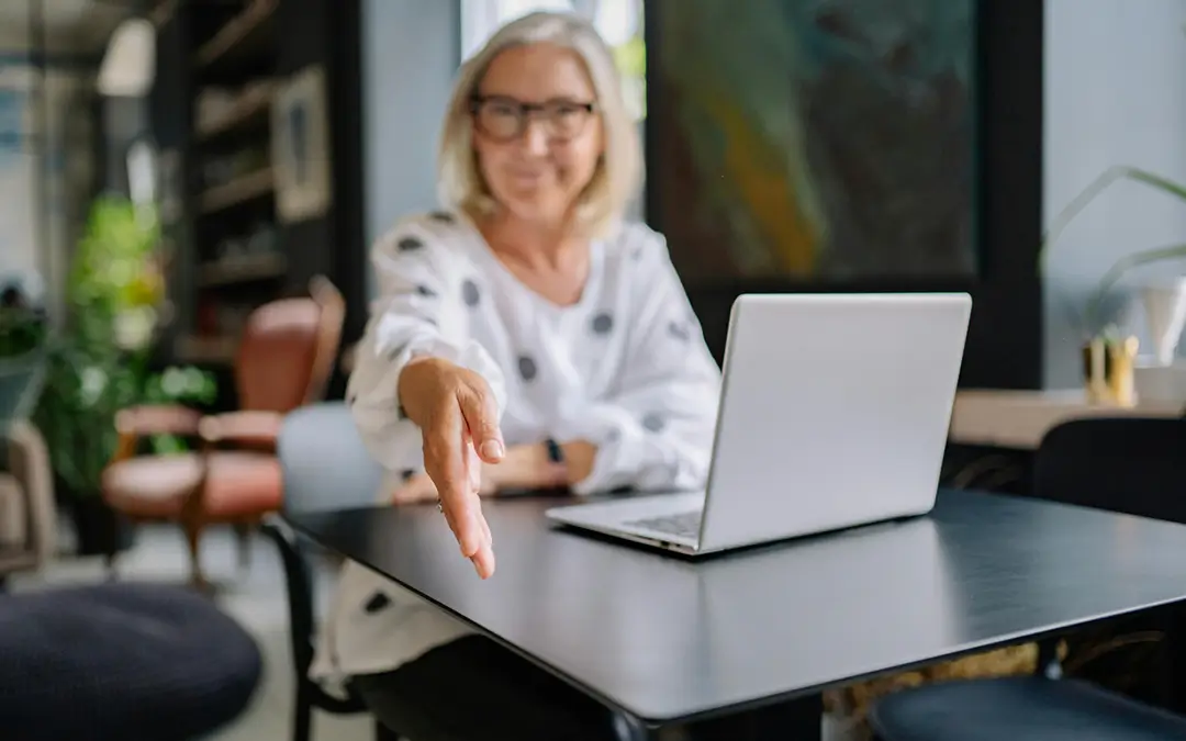 mulher de meia idade sentada com laptop, estendendo a mão para cumprimentar