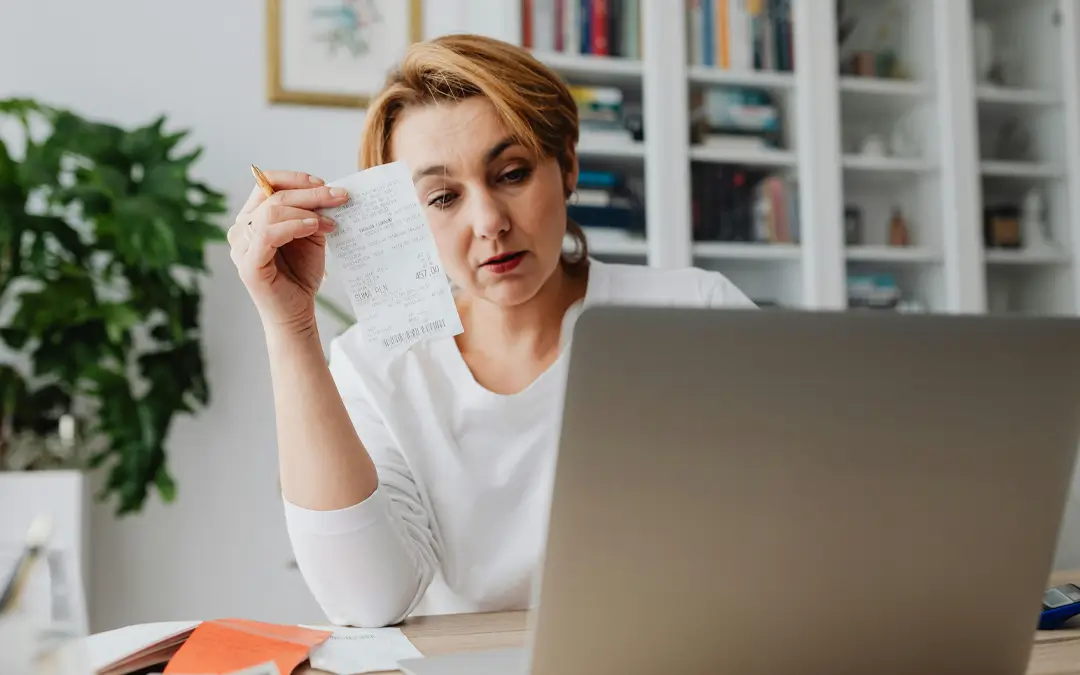 mulher com recibo na mão olhando para laptop