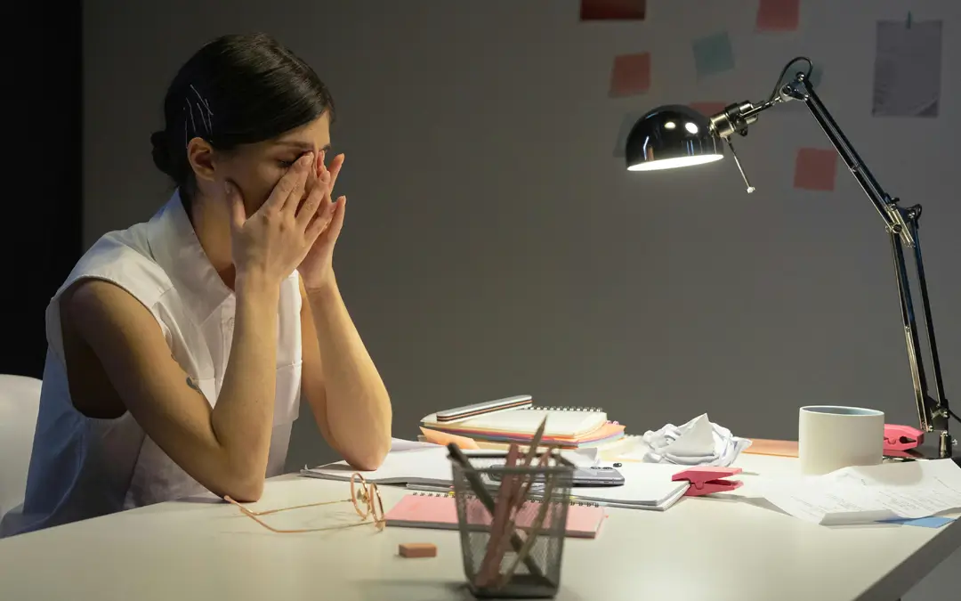 mulher na mesa de trabalho com as mãos nos olhos chorando
