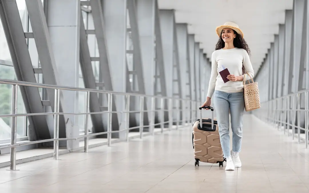 mulher jovem com chapéu puxando a bagagem através do corredor de um aeroporto