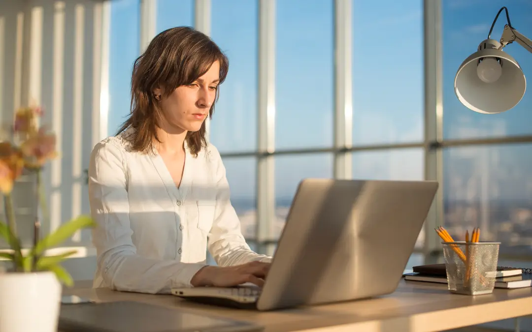 mulher trabalhando no laptop com janela ao fundo com céu azul