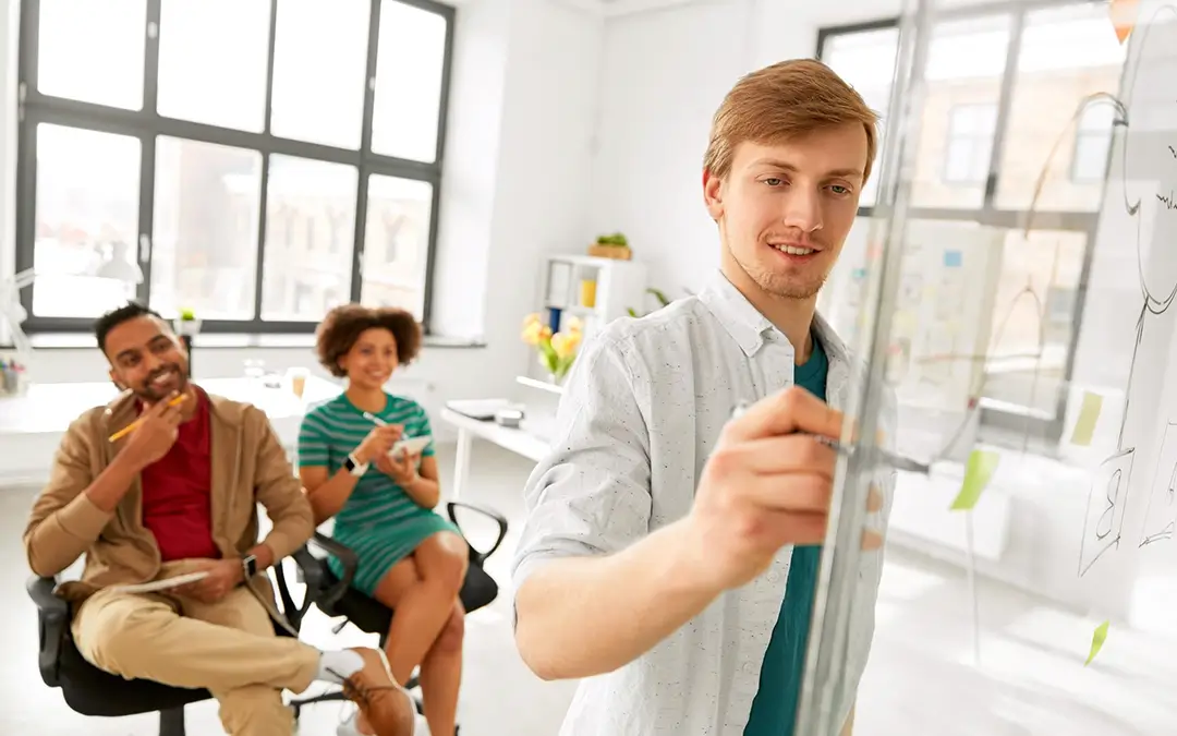 jovem autista escrevendo em painel de vidro com colegas atrás o apoiando