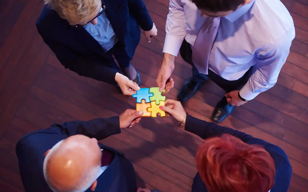 visão de cima de quatro pessoas jutando peças grandes coloridas de um quebra-cabeça