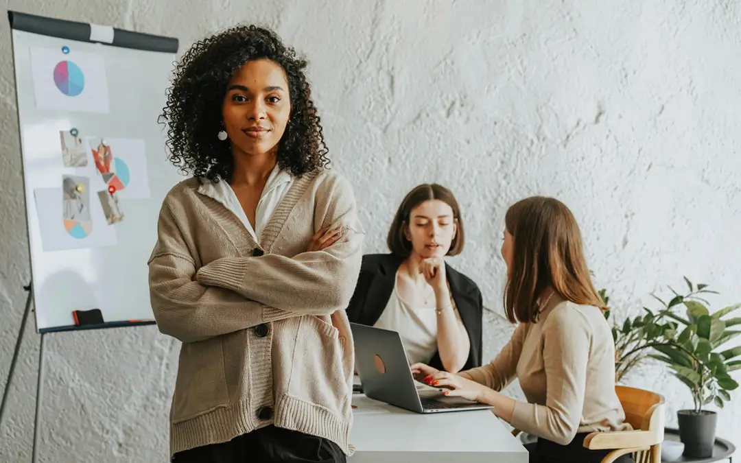 mulher jovem de braços cruzados à frente de flipchart com colegas de trabalho