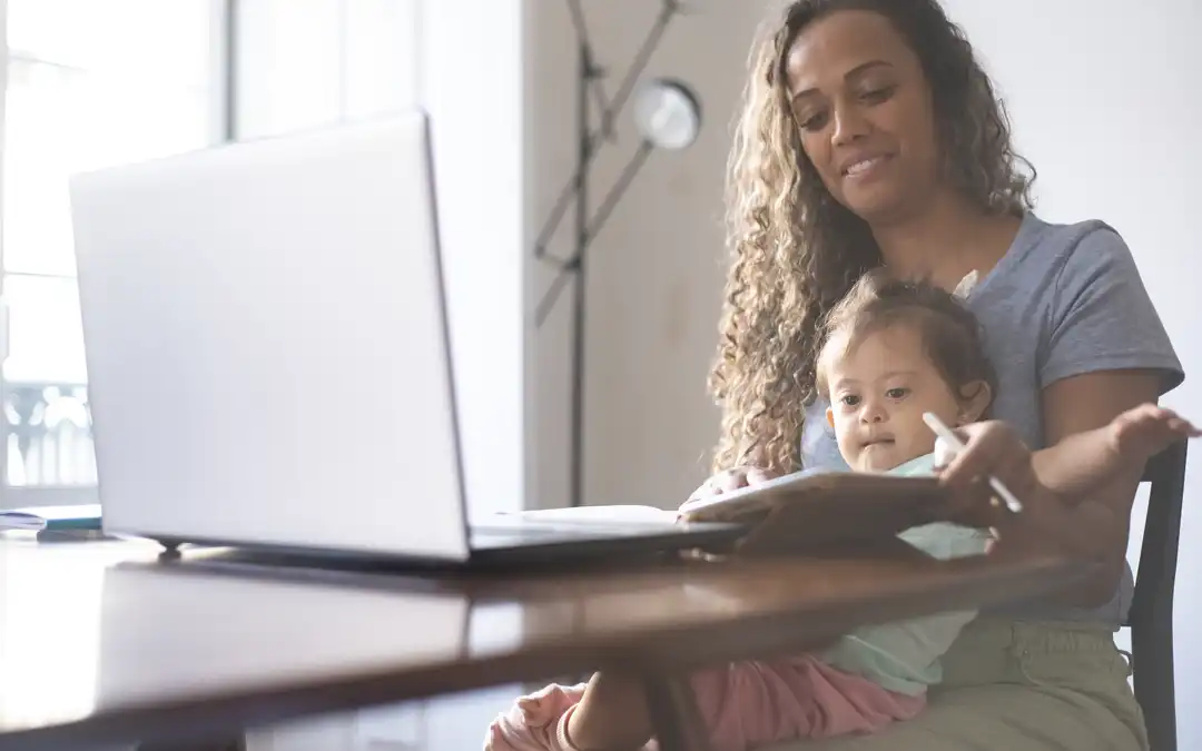 mulher trabalhando em laptop com filho PCD no colo