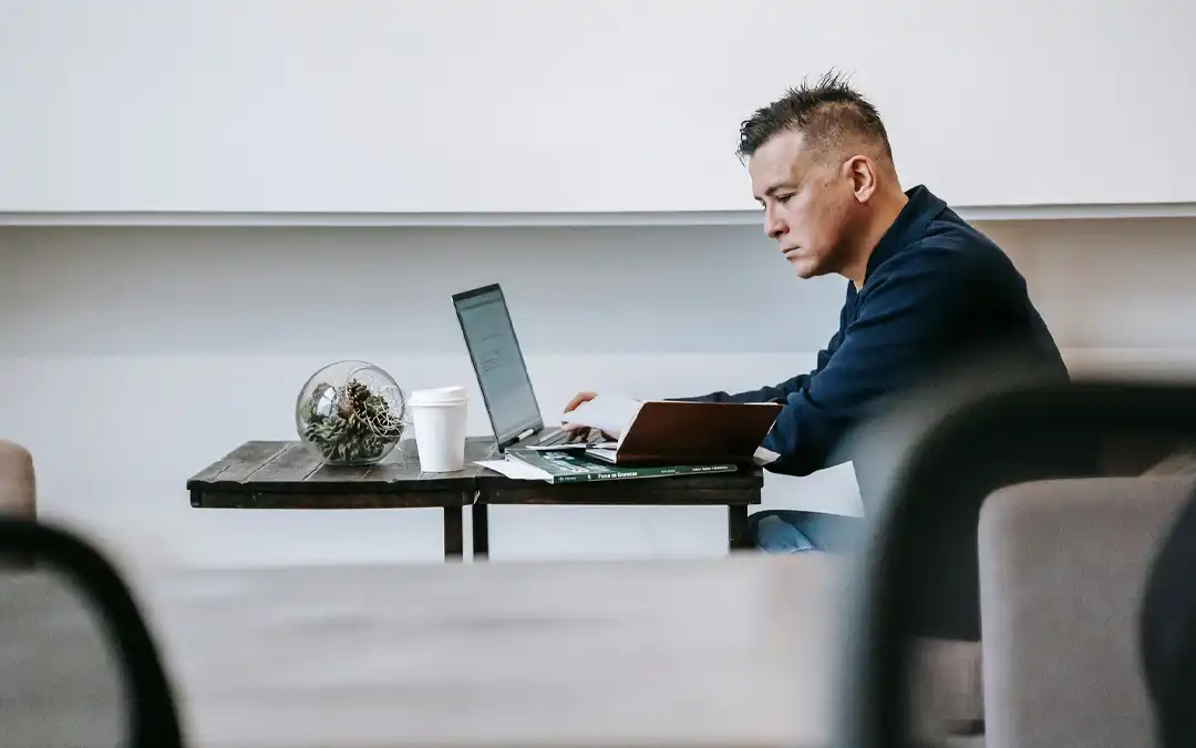 homem trabalhando num laptop numa mesa pequena distante