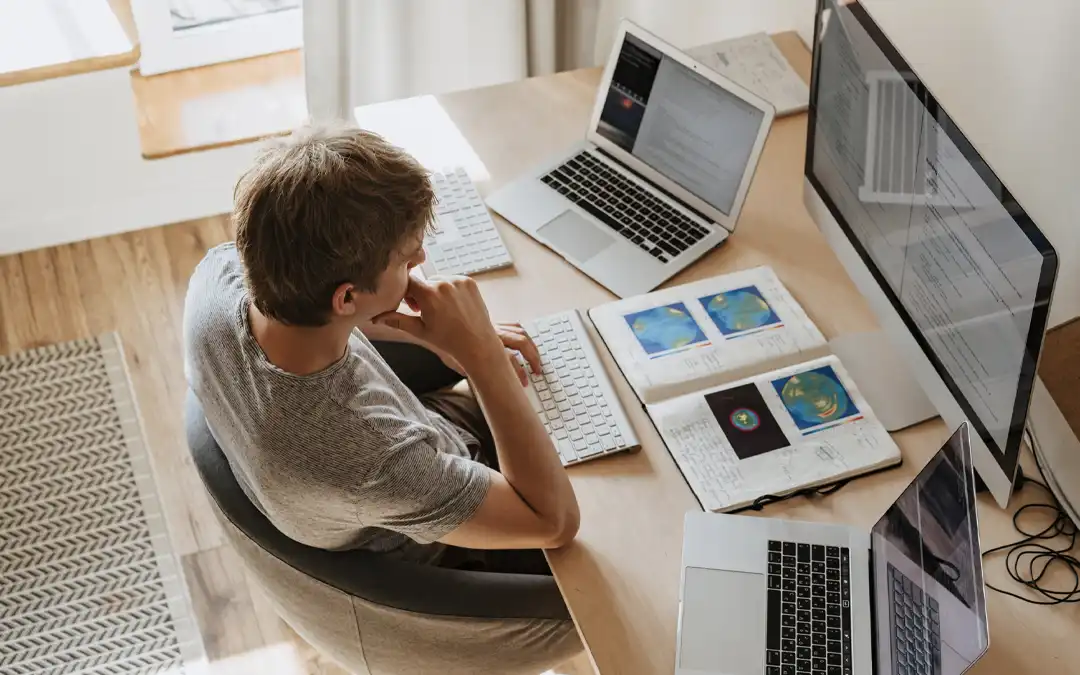 jovem trabalhando com um iMac e dois laptops abertos
