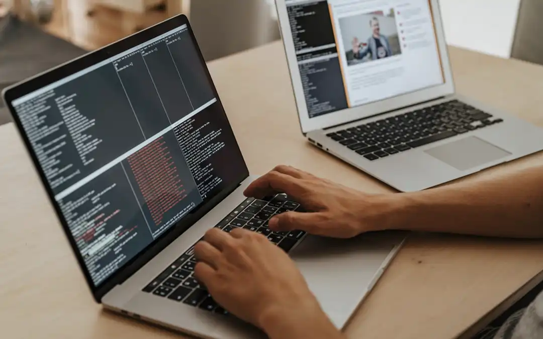 mãos digitando sobre um de dois laptops abertos