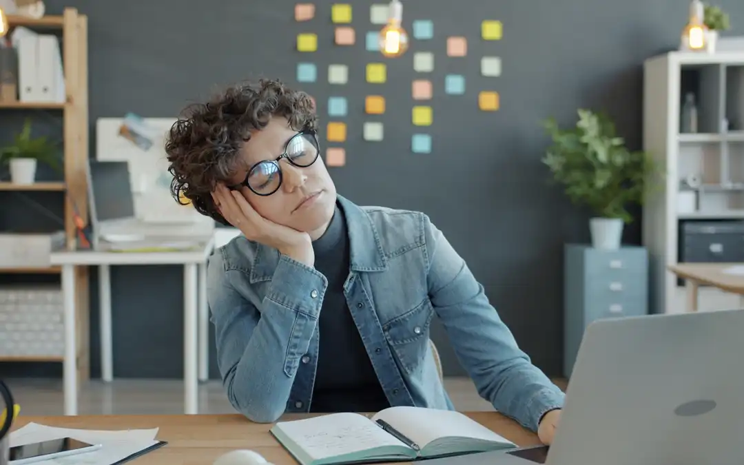 mulher cansada, de frente ao computador, durante o expediente no escritório.